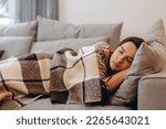 Beautiful serene woman sleeping on comfy sofa under warm cozy plaid in modern living room. Healthy daytime nap, tiredness relief, repose and relaxation during day, lazy weekend at home.