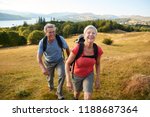 Portrait Of Senior Couple Climbing Hill On Hike Through Countryside In Lake District UK Together