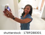 Woman Adjusting Digital Central Heating Thermostat At Home