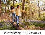 Small photo of Two Children Walking Through Bluebell Woods In Springtime Balancing On Log