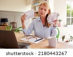 Small photo of Menopausal Mature Woman Having Hot Flush At Home Cooling Herself With Fan Connected To Laptop