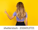 Young beautiful blonde woman wearing sportswear over yellow studio background pointing to object on copy space, rear view. Turn your back