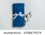 Top view of rolled up blue towel with cotton twig on gray background with copy space.