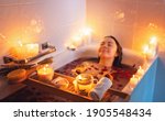 Small photo of Young woman enjoying spiritual aura cleansing rose flower bath with rose petals and candles during full moon ritual. Body care and mental health routine.