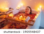 Small photo of Young woman enjoying spiritual aura cleansing rose flower bath with rose petals and candles during full moon ritual. Body care and mental health routine.