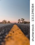 Small photo of Road less traveled, low angle viewing the yellow double lines in the desert or outdoor area. Sunset hours lighting the black paved road and mountains. Road goals to get somewhere. Joshua Tree.