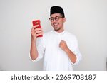 Small photo of Moslem Asian man clenched fist showing excitement when looking to his mobile phone
