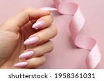 Girl`s hand with a beautiful long nails covered by light pink polish on a pink background with ribbon