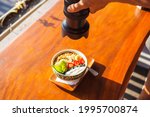 A tasty delicious fruity smoothie bowl on a wooden tray, filmed by anonymous photographer. Shooting for photobanks in a sun lit restaurant. Yummy breakfast made from yoghurt, muesli and tropical fruit