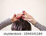 woman is doing her hair, straightened, combing, the disheveled bun on her head.  Dark hair is tied with a transparent spiral elastic band. Modern fast hairstyle. Cares about a beautiful hair. Copyspac