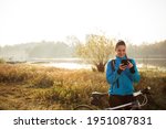 Smiling, happy young Caucasian woman taking a break during early morning mountain bike ride along the lake shore, typing messages on smart phone