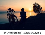 Inspirational view caucasian male cyclist sit by touring bicycle looking to scenic relaxing golden sunset background by sevan lake in Armenia. Bicycle touring lifestyle concept