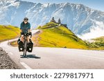 Cyclist back view on the road in scenic caucasus nature with Gergeti trinity monastery in the background. Traveller on bicycle. Solo travel long distance bicycle touring concept