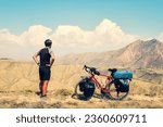 Back view caucasian male cyclist standing by red touring bicycle looking to scenic mountains background. Active inspirational lifestyle concept