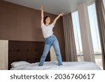 Happy young woman having fun and dancing on the bed in the bedroom. Bottom view. Indoor.