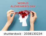 Small photo of World Alzheimer's day. Female's hands unravel the tangled red threads on the silhouette of the head, representing the brain. Blue background. Flat lay. The concept of mental health.