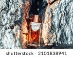 Small photo of A glass transparent rectangular bottle of golden perfume lying in a crevice of a gray marble stone. Perfumes and cosmetics