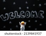 Mars colonization. Figure of astronaut with victoriously raised hands. In the background, a chalky black board with the inscription welcome. Close up.