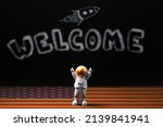 Mars colonization. Figure of astronaut with victoriously raised hands. In the background, a chalky black board with the inscription welcome and a flying rocket, a floor with an American flag design.
