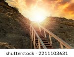 Religion and motivation. A wooden steep staircase in the mountain leading to the sky, with bright sunlight and sunset. Bottom view. The concept of paradise, victory and hope for a bright future.