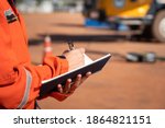 Small photo of Action of safety officer is taking note on checklist with blurred background of crane truck vehicle. Safety inspection audit in heavy operation concept photo, selective focus at the person's hand.