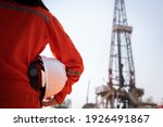 Small photo of A worker is holding safety hardhat or helmet with blurred background of drilling rig derrick structure, selective focus at hardhat. Ready to working in oil field industrial concept photo.