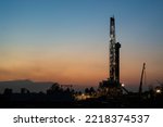 Small photo of Oil field drilling rig derrick structure on dusk sky background. Industrial and business operation scene