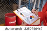 Small photo of Action of safety officer is checking chemical hazard material form for correct the oil spill kit which is placed at front of chemical storage warehouse area in factory. Close-up and selective focus.