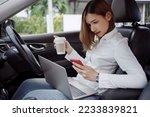 Young woman using smartphone and drinks coffee inside a car. Multitasking.