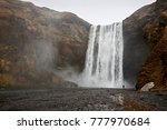 Small photo of A single man stares up at the gargantuan waterfall Skogafoss, Iceland