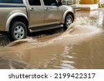 Small photo of Pickup truck passing through flooded road. Driving car on flooded road during flood caused by torrential rains. Flooded city road with large puddle. Splash by car through flood water. Selective focus.