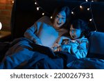 Asian mother and daughter reading bedtime stories in bedroom smiling and home atmosphere at night