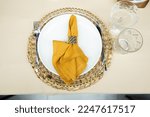 Small photo of Table set with an orange napkin and gold holder and sheaf of wheat spoon and two glasses