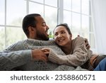 Cheerful young asian woman in sweater hugging and talking to african american boyfriend at home