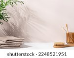 Small photo of Сlean bathroom background with green palm branch that casts shadows, terry cotton towels and bamboo brushes. Mockup space for presentation of beauty products