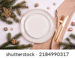 Stylish table setting, fir branches, star and balls with white plate, cutlery and beige napkin on white table. Christmas concept. Top view, flat lay.