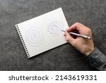 A man with trembling hands is trying to repeat the spiral drawing in a notebook. Test for essential tremor and parkinson