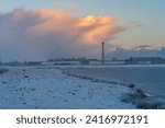 Small photo of Brake, Germany - January 18, 2024: cloud in scenic light of the rising sun over the factory REHAU, a mobile phone mast and the Kleiputte biotope on a snowy winter day