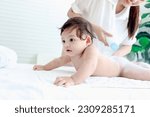 Small photo of Happy toddle baby infant child lying on white towel after bathing in bathroom, mother holding dusting powder bottle, mom applying talcum powder on body of her daughter kid, childhood and parent care.