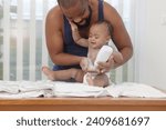 Small photo of Happy African family, toddle baby infant sitting on towel after taking a bath in bathroom, father holds dusting powder bottle and applies talcum powder on body of little cute kid daughter child.