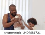 Small photo of Happy African family, father feeds toddle baby infant after take a bath and apply talcum powder on body in bathroom. Little daughter child drinking milk from bottle. Dad and brother son look after kid