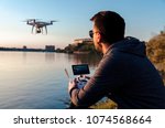 Man operating / flying with drone by the river at sunset , closeup and back view shot 