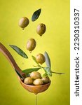 Small photo of ladle with olives and oil on a green background. Olives, extra virgin olive oil and olive leaves float in the air