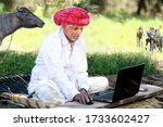 Small photo of Indian old farmer smiles using laptop and internet. Farmer loves technology, Old farmer works on Laptop. Smile of Knowledge. Indian grandpa happy to use laptop. Indian sitting on Cot. Cot in Farm.