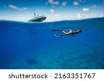 Small photo of Split shot of snorkeler swimming at the surface of a tropical coral reef with a super yacht tender above for safety on a sunny day with clear waters in Fakarava atoll, French Polyesia