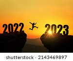 Man jumping on cliff 2023 over the precipice at amazing sunset. New Year's concept. Symbol of starting and welcome happy new year 2023. People enters the year 2023, creative idea