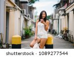 Portrait of a young, athletic, attractive and cute Chinese Asian girl using her smartphone on a street in Asia during the day. She is tanned, petite and relaxed. 
