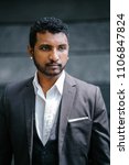 Small photo of Head shot portrait of a young Indian man in a 3-piece suit and pocket square. He is sporting a beard and diamond earrings which makes him roguish and cool.