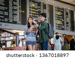 A young, attractive interracial Asian couple are finding their way to their flight in an airport. The Korean man is pointing the way to his Indian girlfriend in front of the flight information display
