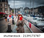 Small photo of Honfleur, France July 2021. A woman with a phone in a red case takes a picture, pandemic time people in massacres, a woman is facing the camera